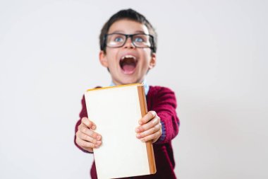 Elinde kitap olan süveter giymiş bir çocuk kameraya göstererek bağırıyor. Kavramsal. Boşluğu kopyala.