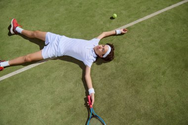Beyaz elbiseli ve kırmızı ayakkabılı genç bir tenisçi yeşil çimen kortunda bitkin bir şekilde yatıyordu. Yanında raket ve tenis topu vardı. Sporda azim ve çabayı somutlaştırıyordu..