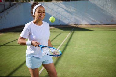 Güneşli bir kortta tenis oynayan neşeli bir kadın. Elinde bir raket var, oyuna hazır. Sahne neşe, açık hava aktivitesi ve sağlıklı bir yaşam tarzını resmediyor..