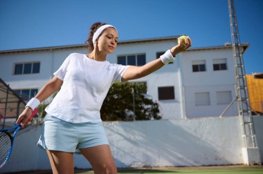Genç bir kadın güneşli bir tenis kortunda hizmet etmeye hazırlanıyor. Sportif ve adanmış bir tutum sergileyen sahnede atletizm, odaklanma ve aktif bir yaşam tarzı vurgulanıyor..