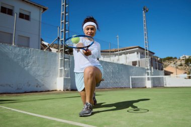 Güneşli bir günde açık hava kortunda tenis oynayan enerjik bayan sporcu. Etkin spor ve spor etkinlikleri için marifetli bir zanaat ve canlı bir coşku gösterisi..