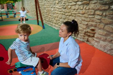 Bir anne ve küçük oğlu parlak renkli bir oyun parkında oynuyorlar. Ortam canlı, canlı renkler ve eğlence odaklı, sıcaklık, mutluluk ve aile bağlarını çağrıştırıyor. Çocukluk, ebeveynlik ve bağlantı temaları için uygun.