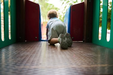 Renkli bir oyun parkındaki bir tünelde sürünen küçük bir çocuk görülüyor. Görüntü, açık havada neşeli bir oyun, keşif ve keşif anını yansıtıyor..