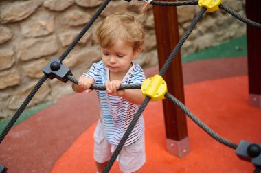 Açık hava oyun sahasında ip tırmanma yapısını keşfeden, aktif oyun ve bina koordinasyonunu sağlayan küçük bir çocuk..