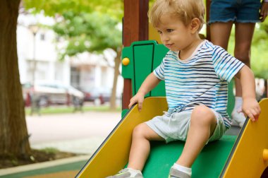 Bir çocuk dışarıda oynuyor, oyun parkında kayıyor. Yeşil çevre ve neşeli aktivite çocukluk eğlencesi ve canlı keşifler sergiliyor.