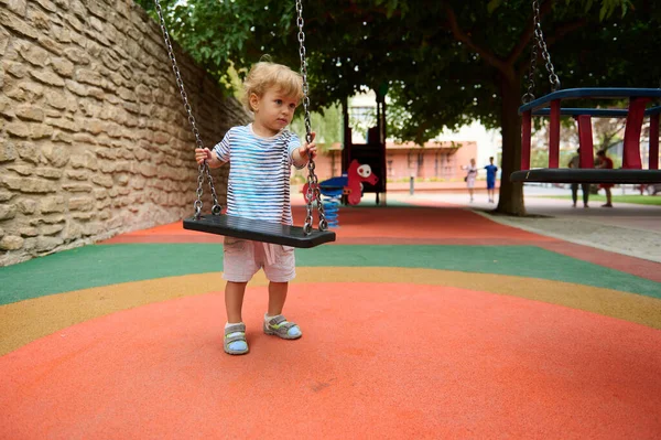 Genç bir çocuk, renkli ekipman ve yeşilliklerle çevrili canlı bir oyun alanında salıncakta sallanıyor. Neşeli atmosfer yaratıcılığı ve dışarıdaki eğlenceyi teşvik eder. Çocuklar ve aileler için mükemmeldir..