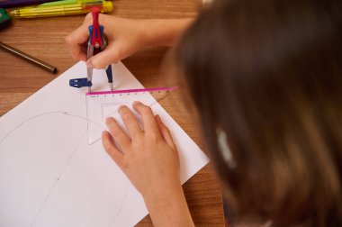 Masada geometrik çizim üzerinde çalışan bir öğrenci pusula, cetvel ve kağıt kullanıyor..