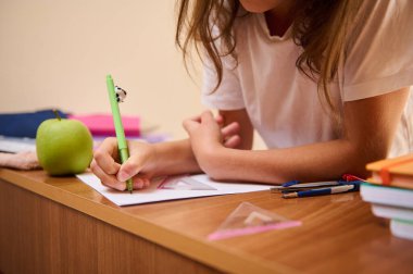 Genç bir öğrenci staj ve çalışma araçlarıyla bir masada ev ödevi sorunları çözer. Ahşap masanın üstünde akademik çevreyi vurgulayan bir elma, kalem ve kitaplar görülüyor..