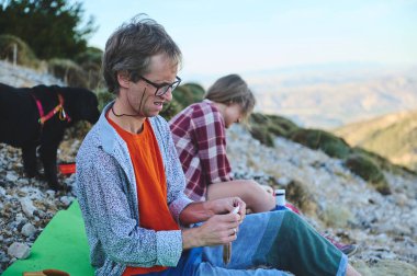 İki arkadaş dağlarda huzur içinde vakit geçirip bir köpek eşliğinde aktif faaliyetlerde bulunuyorlar. Mekan, sakin ve doğal bir ortamda rahatlık ve arkadaşlığın göstergesi. Huzur verici..