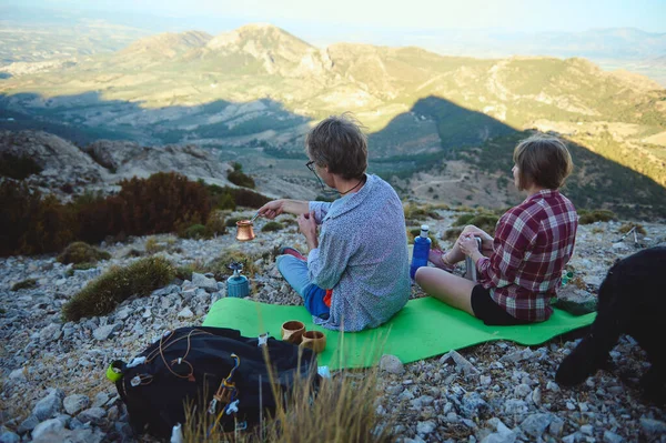Bir çift dağda rahatlar, doğa tarafından çevrelenmiş bir kamp alanından içeceklerin tadını çıkarırlar. Açık mavi gökyüzü ve geniş yuvarlanan düzlükler çarpıcı bir zemin yaratır. Açık hava maceraları için mükemmel..