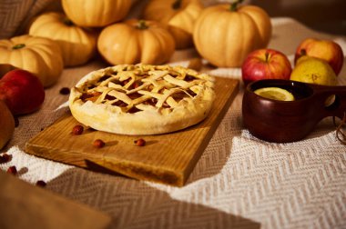 Bir kafes turtası, balkabakları, elmalar, armutlar ve limonlu kupalarla çevrili ahşap bir tahtanın üzerinde oturur. Sıcak sonbahar renkleri Şükran Günü 'nü ve sıcak ev toplantılarını çağrıştırıyor.