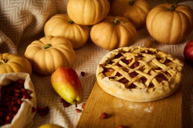 Ahşap bir tahtanın üzerinde kafes turtası, balkabağı, elma ve armut ile sıcak bir sonbahar sahnesi Şükran Günü 'nü, hasadı, aile sıcaklığını ve mevsimsel pişirmeyi çağrıştırıyor..