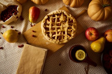 Sıcak bir sonbahar sahnesinde, kabaklar, elmalar, armutlar, kupada bir limon ve kızılcıklarla çevrili ahşap bir tahtanın üzerinde bir kafes üstü turta yer alır. Sıcak, köylü tonları Şükran Günü anılarını ve aile toplantılarını anımsatıyor, rahatlatıcı mevsimsel bir hava yaratıyor..