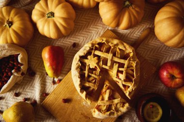 Sonbahar hasat sahnesinde kafes şeklinde balkabağı turtası, küçük balkabakları, elmalar ve armutlar sıcacık bir örtüde. Şükran Günü için mükemmel, aile toplantıları ve ev yapımı..