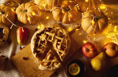 Sıcak bir sonbahar Şükran Günü sahnesi ahşap bir tahtanın üzerinde kafes turtası, balkabağı, elma ve peri ışıkları ile sıcak bir hasat havası yaratıyor..