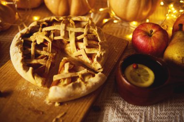 Ahşap bir tahtanın üzerinde kafes turtası, elma, armut ve limonun olduğu ılık bir sonbahar sahnesi, parlak ışıklar ve samimi bir Şükran Günü havası..