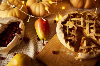 Kafes turtası, elmalar, kızılcıklar, balkabakları ve sicim ışıklarıyla samimi bir sonbahar sahnesi. Sıcak, şenlikli Şükran Günü havası, ev yapımı, aile toplantıları, hasat ve mevsimsel konfor..
