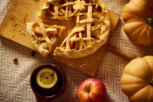 Kırsal sonbahar masasında kafes üstü turta, balkabağı, elma ve limon dilimli bir kupa var. Sıcak, hasat havası Şükran Günü, sonbahar tarifleri ve mevsimlik kutlamalar için ideal..