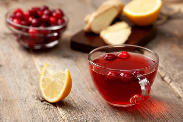 cranberries lemon ginger drink in a glass cup, honey, half a lemon, slices of ginger on old wooden background