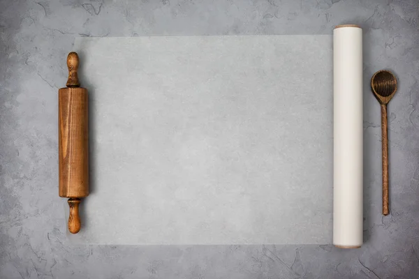 paper for baking, wooden rolling pin on a gray concrete background. view from above. copy space