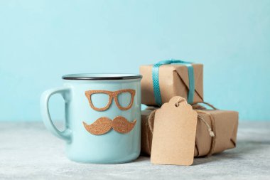 Babalar Günü hediyesi konsepti. Mavi arka planda, bıyıklı, gözlüklü ve hediye kutulu mavi kupa.