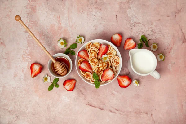 パンケーキシリアル ピンクの背景に新鮮なイチゴ ミルクと蜂蜜とミニパンケーキ 上からの眺め ストック写真