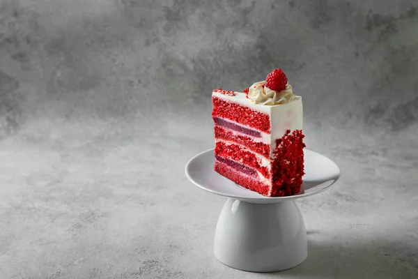 piece of red velvet cake on a white plate on a gray concrete background