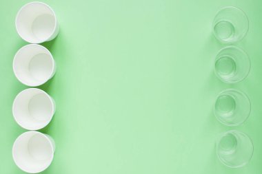 Beyaz kağıt ve plastik tek kullanımlık bardakların yeşil arkaplanındaki düzen. Çevreye önem vermek. Çöplerin geri dönüşümü ve sıralanması. Tek kullanımlık sofra takımı. Çevre kirliliği.