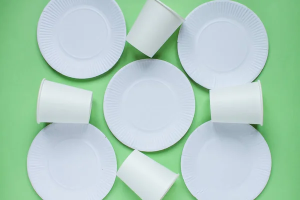 The layout on a green background from paper disposable plates. Caring for the environment. Recycling and sorting of garbage. Disposable tableware. Environmental pollution....