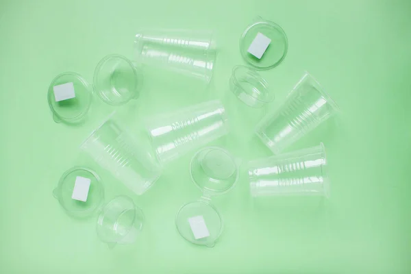 Tek kullanımlık beyaz plastik bardakların yeşil arka planının çizimi. Çevreye önem vermek. Çöplerin geri dönüşümü ve sıralanması. Tek kullanımlık sofra takımı. Çevre kirliliği.