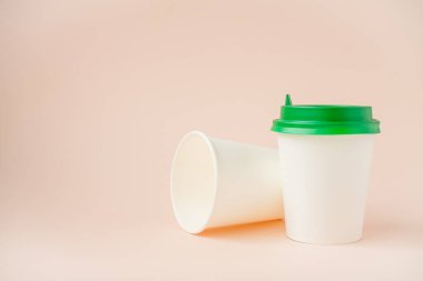 Açık pembe arka planda plastik kapaklı tek kullanımlık kağıt bardaklar. Ekoloji, sıfır atık kavramı. kopyalama alanı.