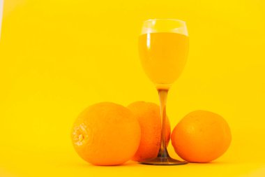 Parlak sarı arka planda parlak portakallar ve bir bardak portakal suyu. Sağlıklı yaşam tarzı kavramı.