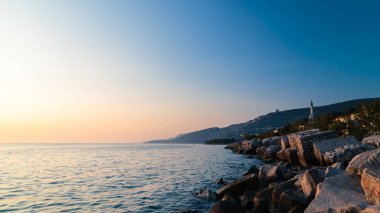 Trieste, Friuli Venezia Giulia, İtalya'nın deniz feneri altında sahilde günbatımı