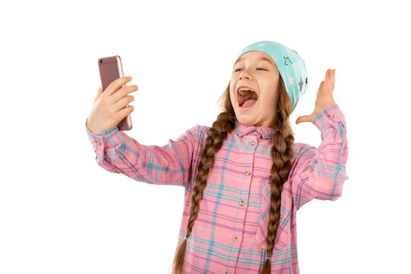 Förvånad över liten flicka håller mobiltelefon isolerad på vit bakgrund. Spel, barn, teknik koncept — Stockfoto