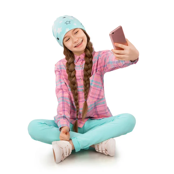 Leende liten flicka håller mobiltelefon och göra selfie isolerad på vit bakgrund Stockbild
