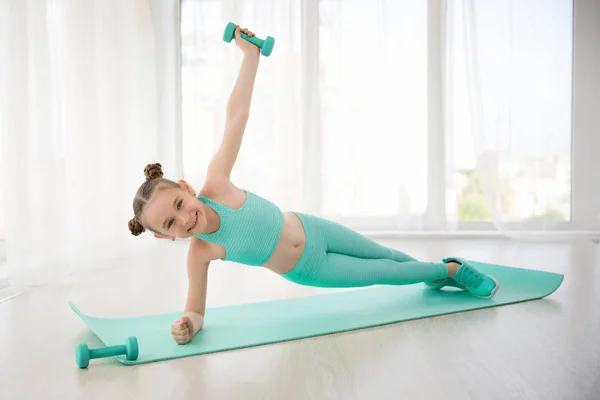 Pequeña gimnasta de chica deportiva en ropa deportiva haciendo ejercicios en una alfombra interior —  Fotos de Stock