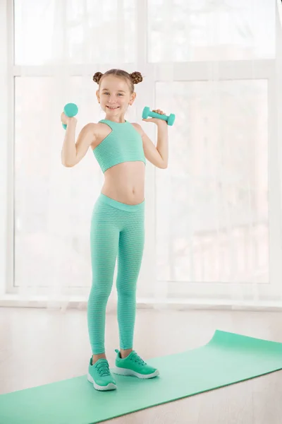 Pequeña gimnasta de chica deportiva en ropa deportiva haciendo ejercicios en una alfombra interior Fotos De Stock Sin Royalties Gratis