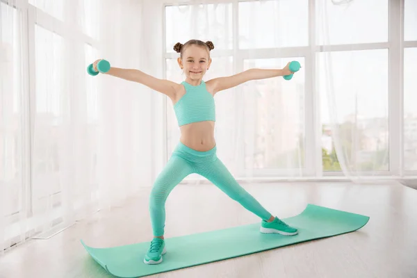 Pequeña gimnasta de chica deportiva en ropa deportiva haciendo ejercicios en una alfombra interior Imágenes de stock libres de derechos