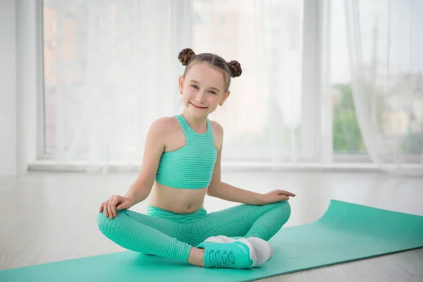 Pequeña gimnasta de chica deportiva en ropa deportiva haciendo ejercicios en una alfombra interior Imagen de archivo