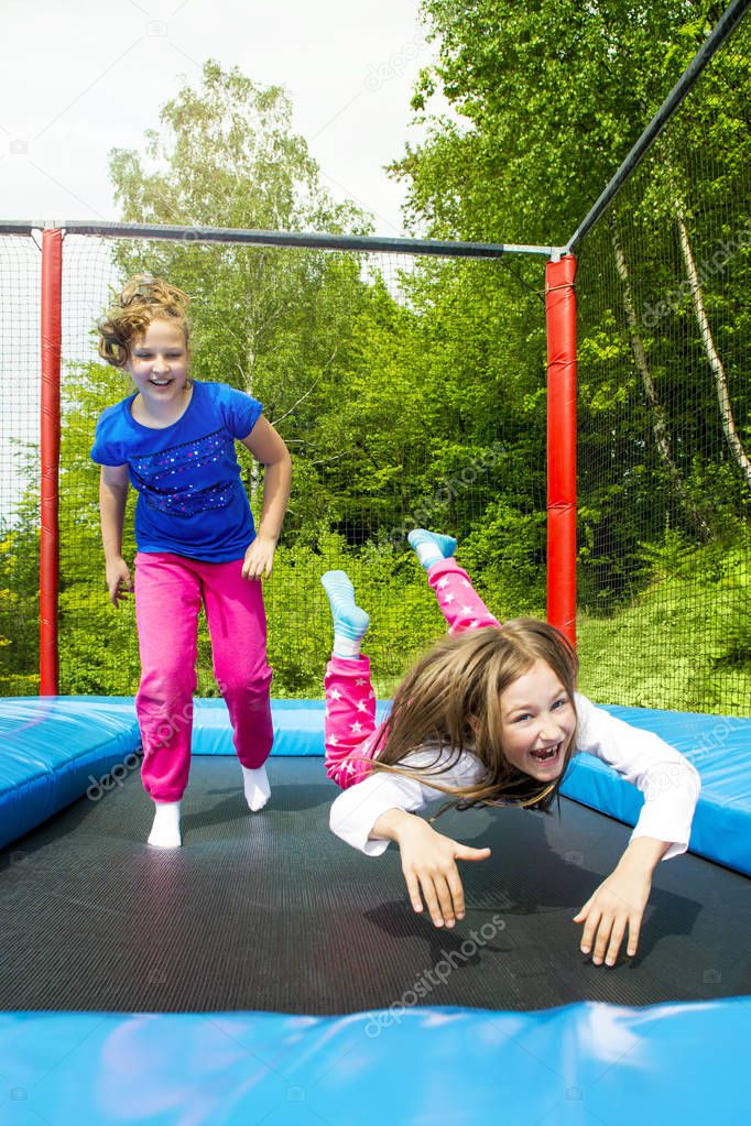 Happy girls jumping high on a trampoline on a sunny day outdoors.