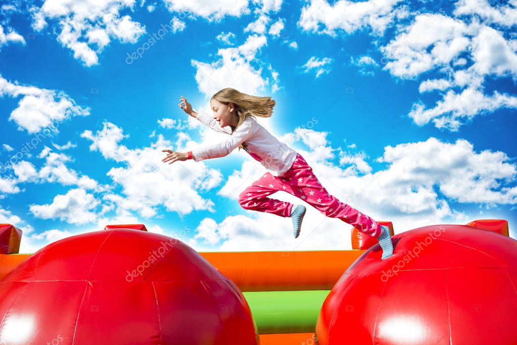 Happy little girl having lots of fun while jumping from ball to ball on an inflate castle.