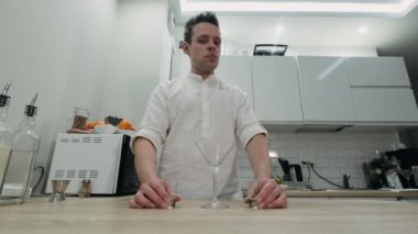 Alkollü kokteyl yapıyorum. Barmen evde tezgahın arkasında duruyor ve kameraya bakıyor.