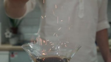 Barmen yanan bir alkollü kokteylin üzerine tarçın serper.