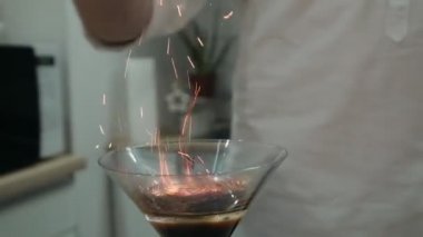 Barmen yanan bir alkollü kokteylin üzerine tarçın serper.