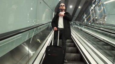 Bagajlı bir adam metro istasyonunda yürüyen merdivenden iniyor.