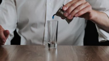 Barmen jigger 'dan bardağa mavi curacao likörü dolduruyor. Kapat.
