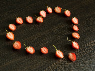 Çilek parçalarından yapılmış kalp şekli koyu ahşap bir yüzeyde açılı..