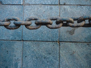 Yukarıdan gelen büyük paslı zincir mavi-gri granit levhaların arka planında yatay olarak görülüyor..