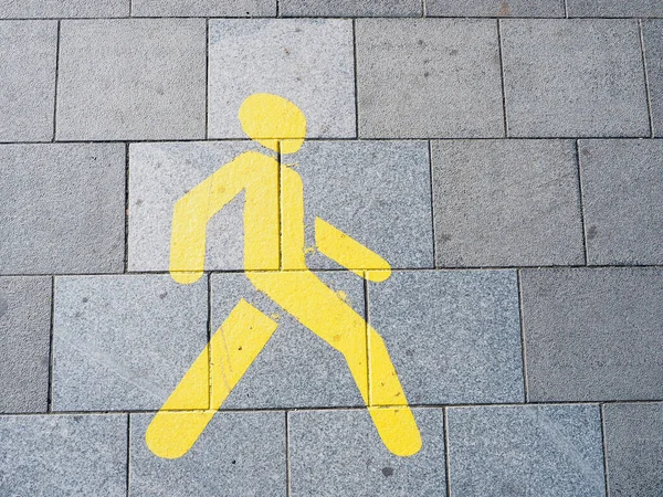 The figure of a yellow man painted with paint on a gray granite sidewalk.