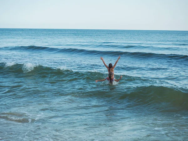 Yazın iki küçük çocuk deniz dalgalarına su sıçratır, arkadan izlerler..